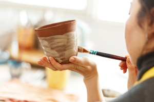 Woman painting clay jug with paint shaping and sculpturing the pottery.