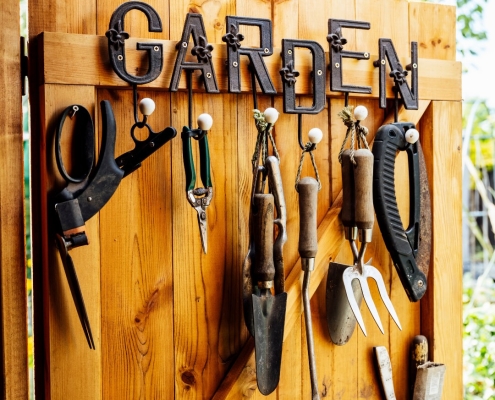 Storage shed wood door with a metal garden sign and hanging garden tools