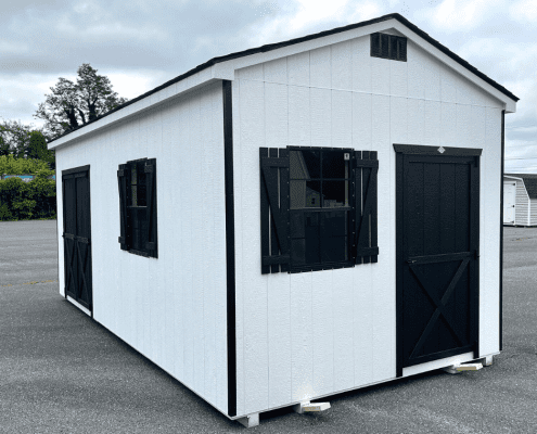 White shed with black shutters and doors on pavement